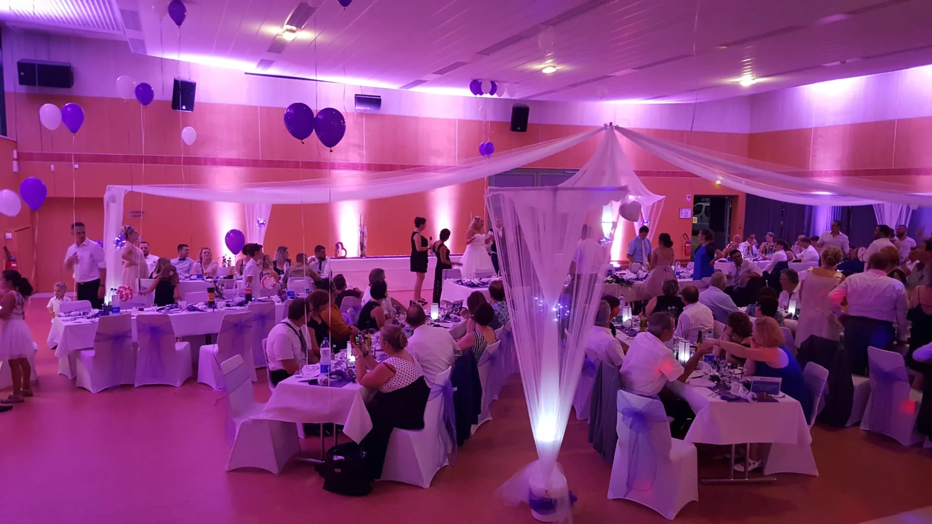 Salle de mariage illuminée en violet avec balcons de tissu blanc